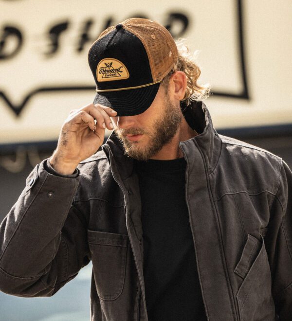 A man in a hat and jacket adjusts his glasses.