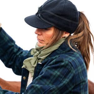 A woman in plaid jacket and hat riding horse.