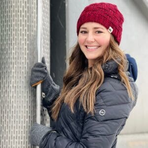 A woman in a red hat and gloves leaning on a wall.